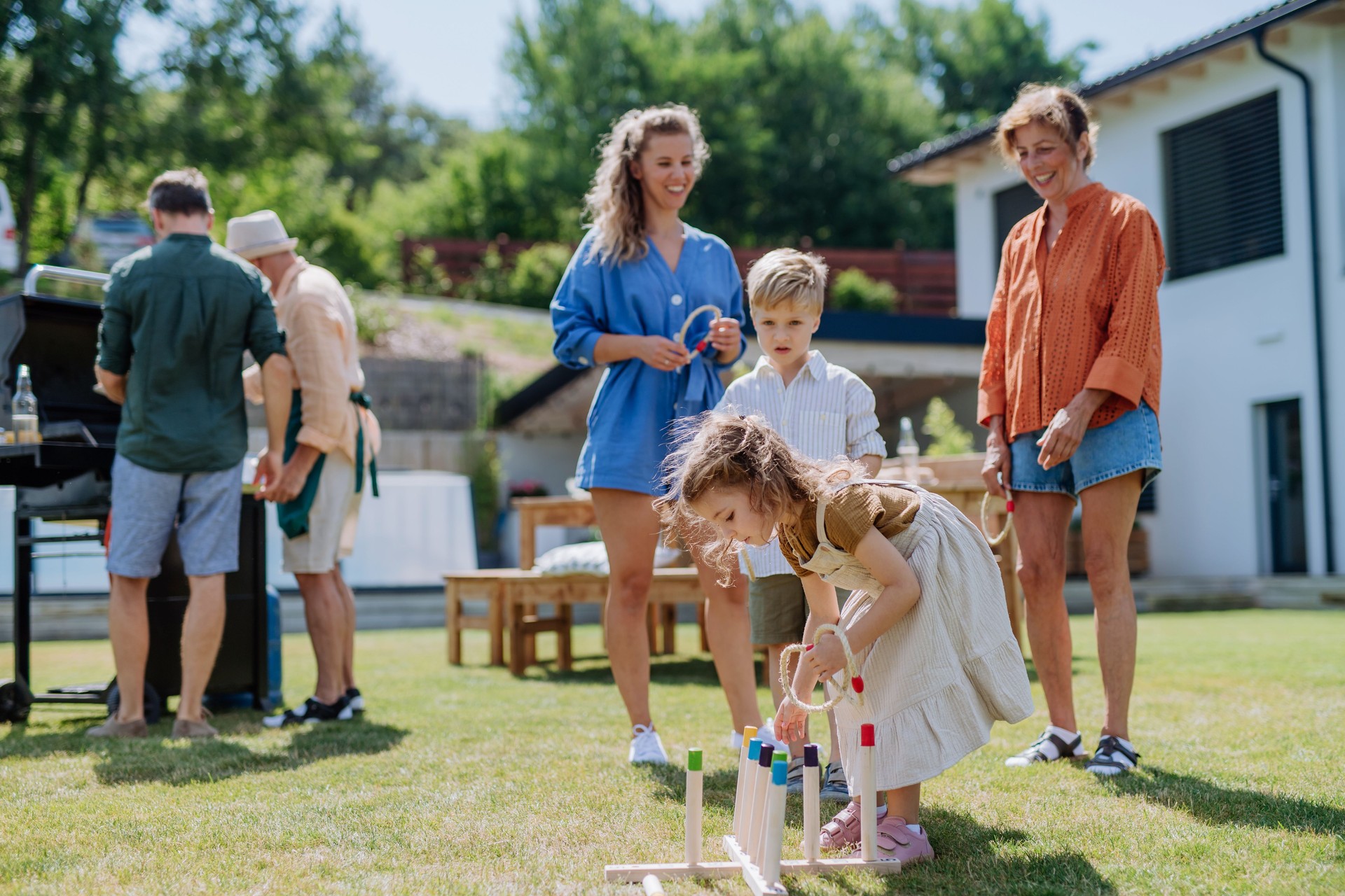 Multi generation family playing throw a ring game when grilling outside on backyard in summer at garden party.